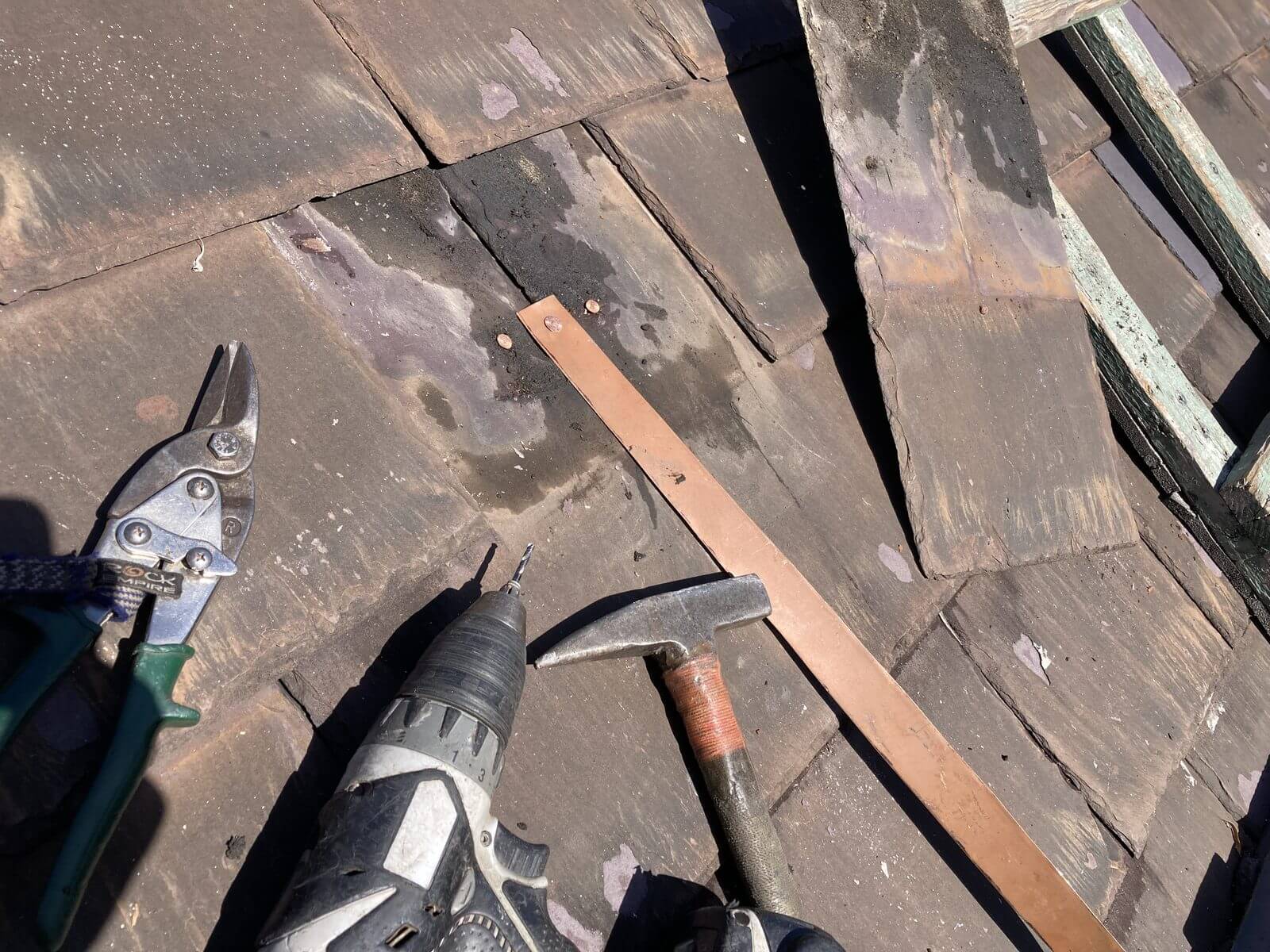 Copper strip being fitted to a slate roof with hammer, drill and snips